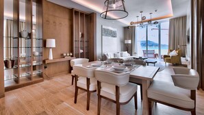Una habitación de hotel moderna con zona de comedor, un ventanal con vistas y una pared de madera con estanterías.