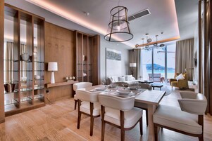 A modern hotel room with a dining area, a large window with a view, and a wooden wall with shelves.