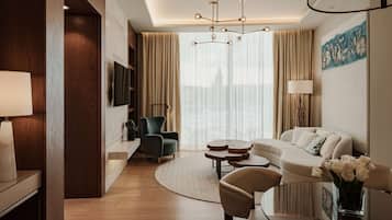 Una habitación de hotel moderna con una pared de acento de madera, un ventanal con cortinas translúcidas, una mesa de centro redonda, un sofá y un televisor montado en la pared.