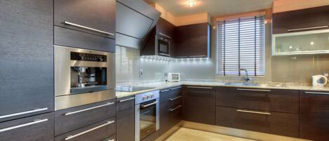 A modern kitchen with dark cabinetry, stainless steel appliances, and a tiled backsplash.