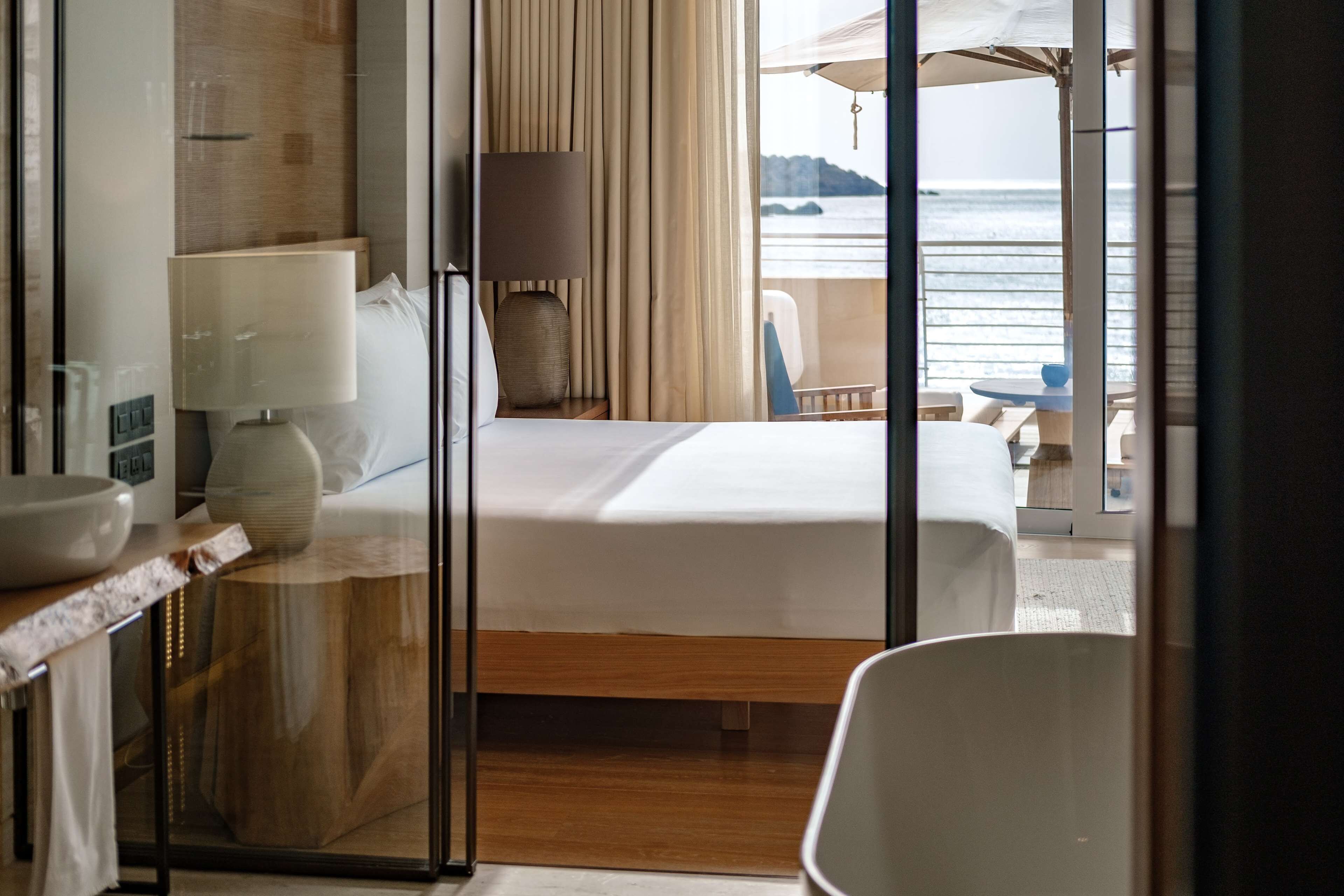 Habitación de hotel con una cama, un escritorio con lámpara, una silla y vistas al mar.