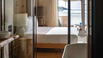 Habitación de hotel con una cama, un escritorio con lámpara, una silla y vistas al mar.