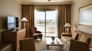 A hotel room with a television, two armchairs, a sofa, a coffee table, and a balcony with curtains.