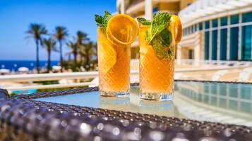 Zwei Gläser mit einem Getränk und Minzblättern, auf einem Tisch vor einem Pool mit Palmen.