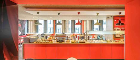 A modern restaurant with a bright red color scheme, a counter with food items, and a seating area with tables and chairs.
