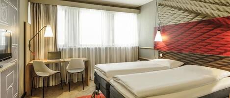 Habitación de hotel con dos camas, un escritorio con silla, un televisor y alfombra roja.