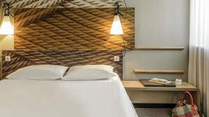 Ett hotellrum med en säng, ett nattduksbord, en lampa och en vävd sänggavel.