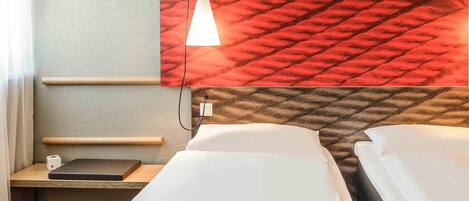 A hotel room with two beds, a desk, a lamp, and a textured wall.