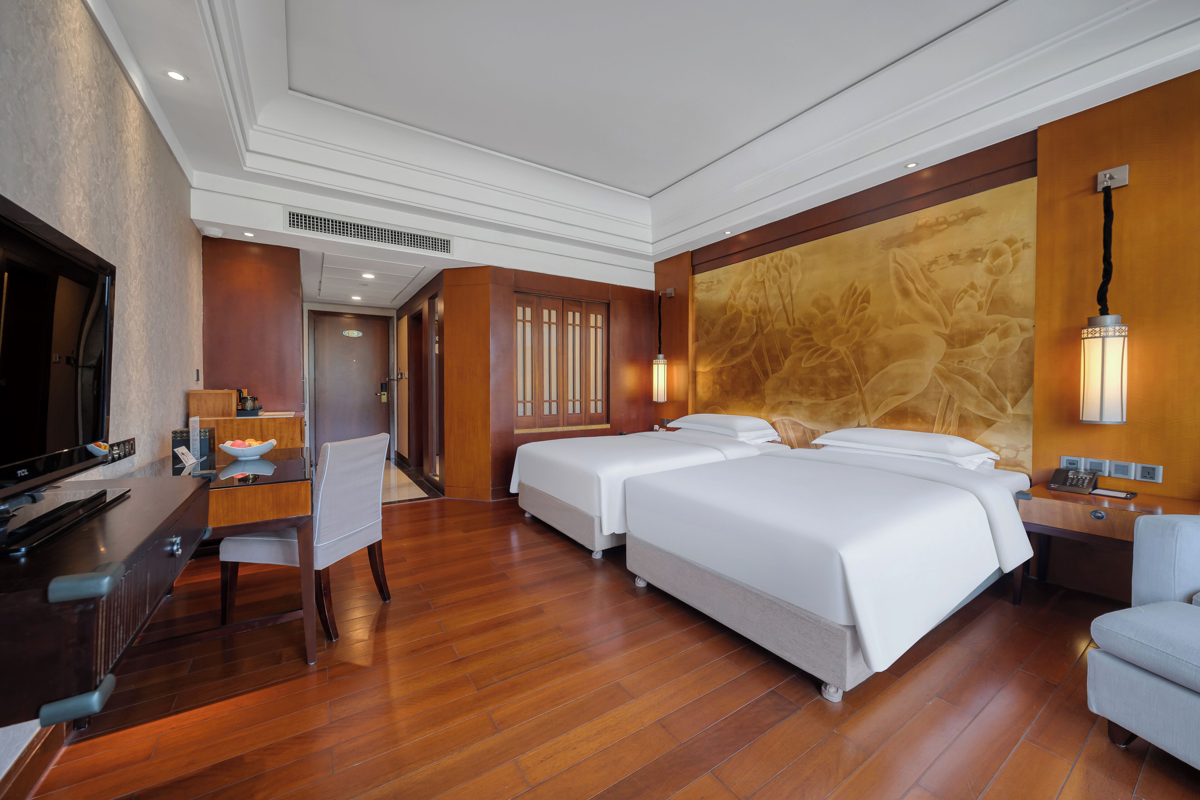 A hotel room with two beds, a desk, a television, and a dining area.