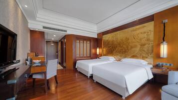 A hotel room with two beds, a desk, a television, and a dining area.