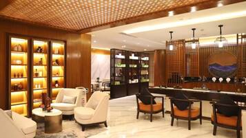 Relax in the stylish lobby, featuring a seating area with sofas and armchairs, a bar with a circular mirror, and decorative shelves.