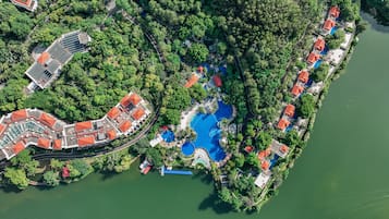 An aerial view of a resort with multiple swimming pools, a large building with a red roof, and lush greenery surrounding the area.