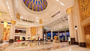 Een ruime lobby met een hoge plafond, grote kolommen en een centrale decoratieve koepel.