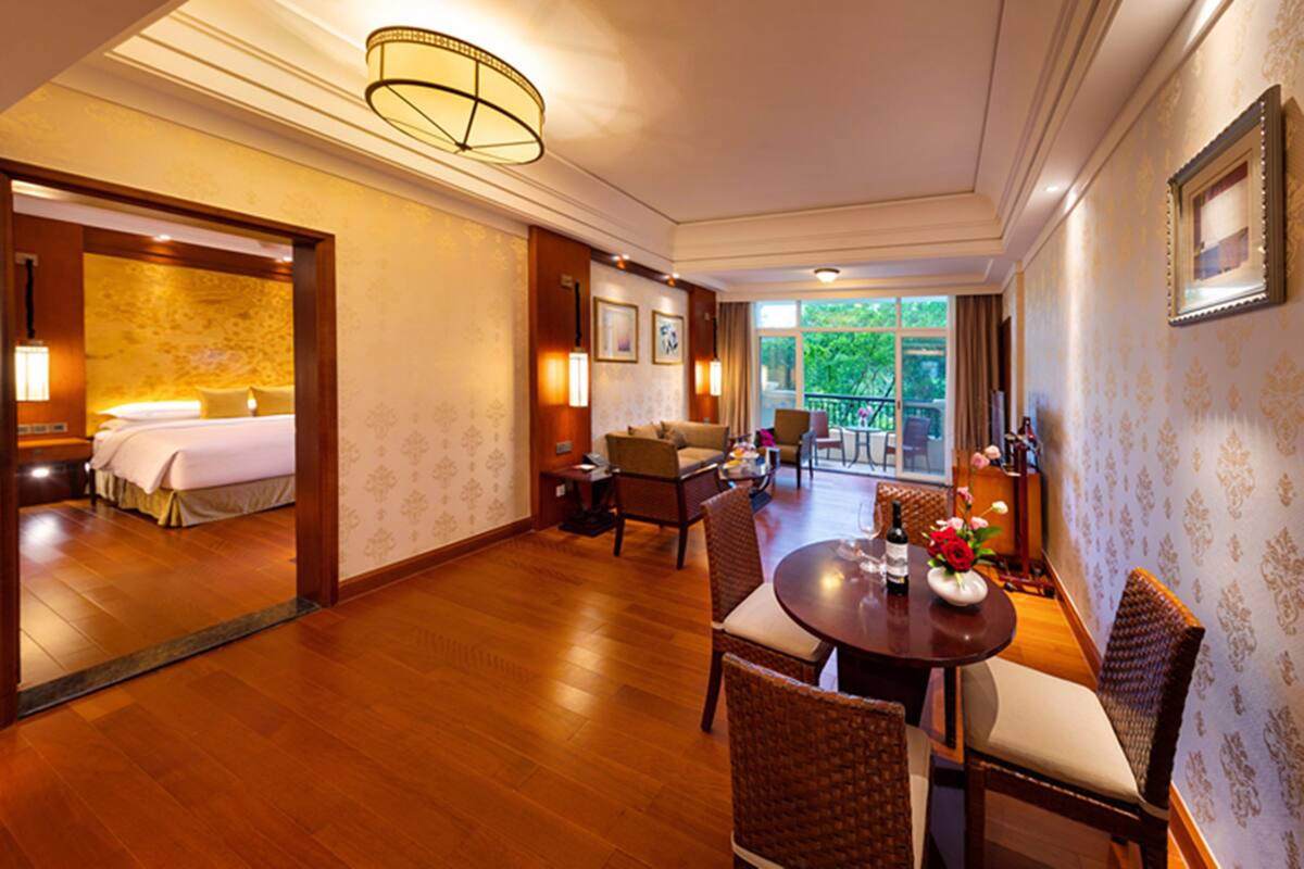 A hotel room with a bed, a dining area with a table and chairs, and a balcony with a view.