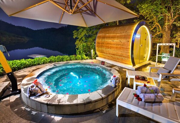 Un jacuzzi con estructura de barril de madera, rodeado de sillas de descanso y una sombrilla.