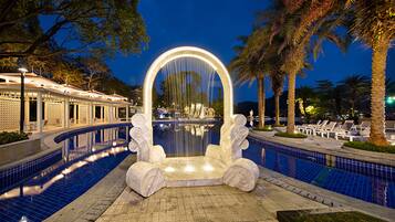 A pool with a central fountain, surrounded by palm trees and lounge chairs.