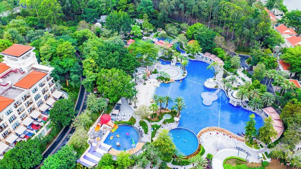 Een luchtbeeld van een resort met meerdere zwembaden, weelderige begroeiing en verschillende gebouwen.