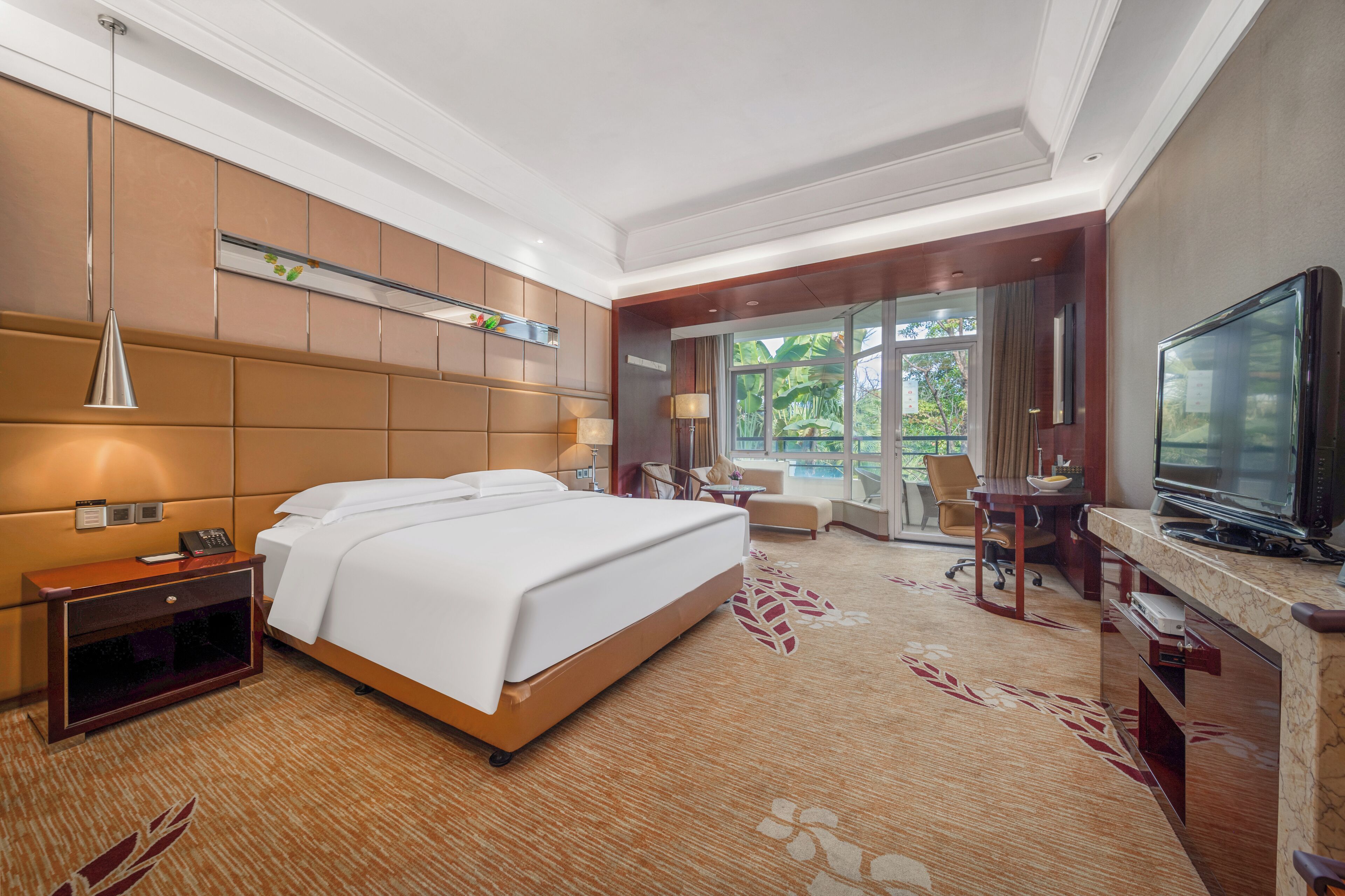 Habitación de hotel con una cama grande, un escritorio con televisor, una lámpara de escritorio, una silla y una ventana con vistas a zonas verdes.