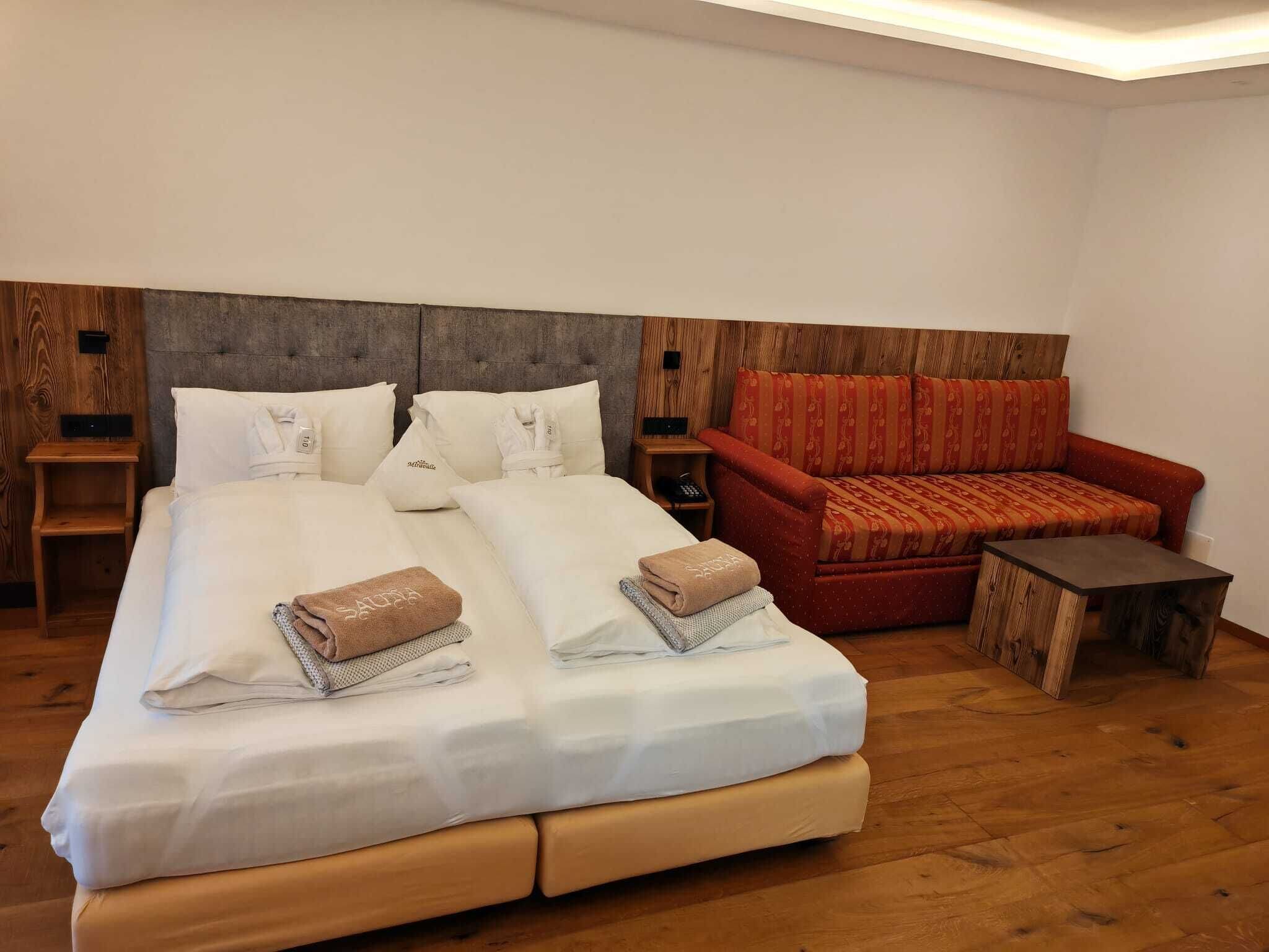 Une chambre d’hôtel avec un grand lit, un canapé rouge, une petite table en bois et une table de chevet avec un téléphone.