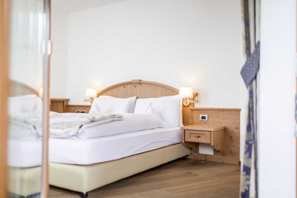 A neatly made bed with white linens, a wooden headboard, bedside lamps, and a small wooden nightstand with a drawer.