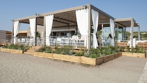 A beachside restaurant with a covered patio, outdoor seating, and wooden planters. - Tombolo Talasso & Beach Resort (Castagneto Carducci)