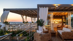 A deck with wicker furniture, a bar area, and a view of the ocean at dusk. - Tombolo Talasso & Beach Resort (Castagneto Carducci)