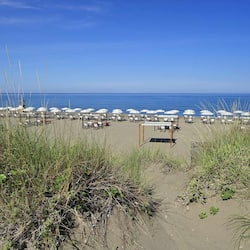 Enjoy beach activities under shaded umbrellas, surrounded by natural dunes and the ocean.