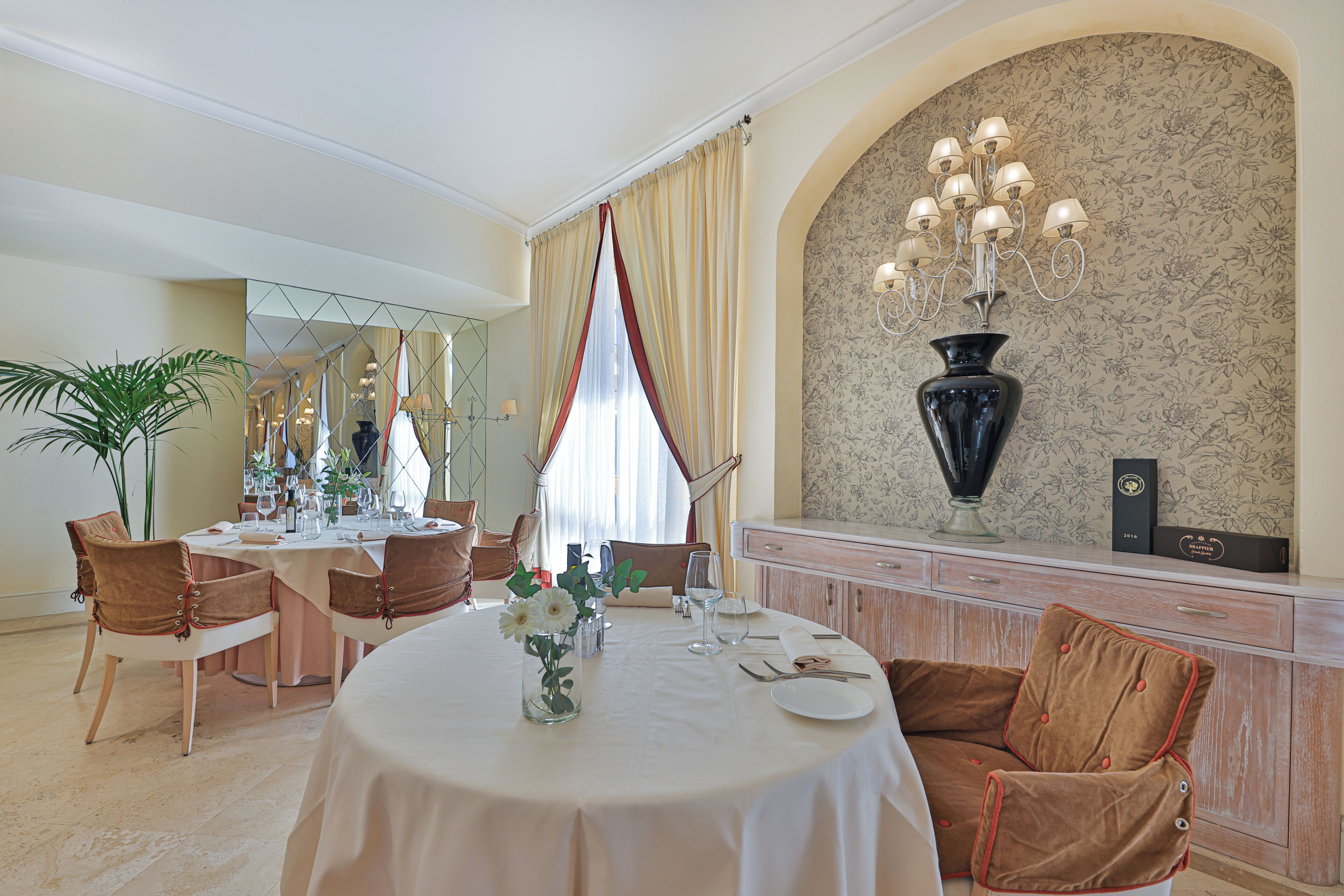 Un comedor formal con una mesa redonda preparada para cuatro personas, un candelabro y un jarrón grande sobre una consola.