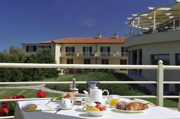 Una mesa de desayuno con cruasanes, fruta y jugo, con vistas a un edificio con balcón.