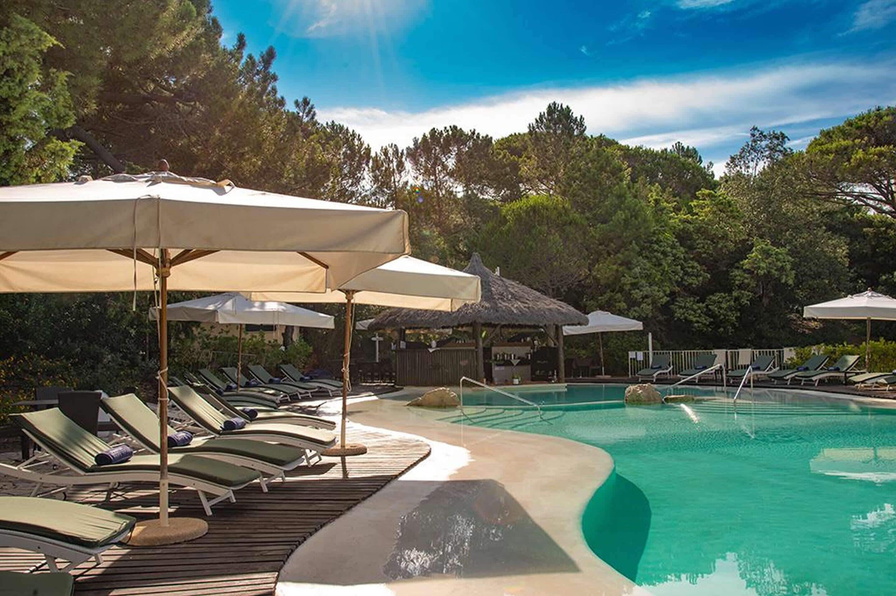 A pool area with lounge chairs and umbrellas, surrounded by trees.