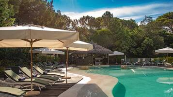 A pool area with lounge chairs and umbrellas, surrounded by trees.