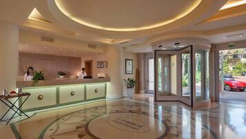 Eine Hotellobby mit einer Rezeption, einem rund gemusterten Boden und einer Glastür zum Außenbereich.