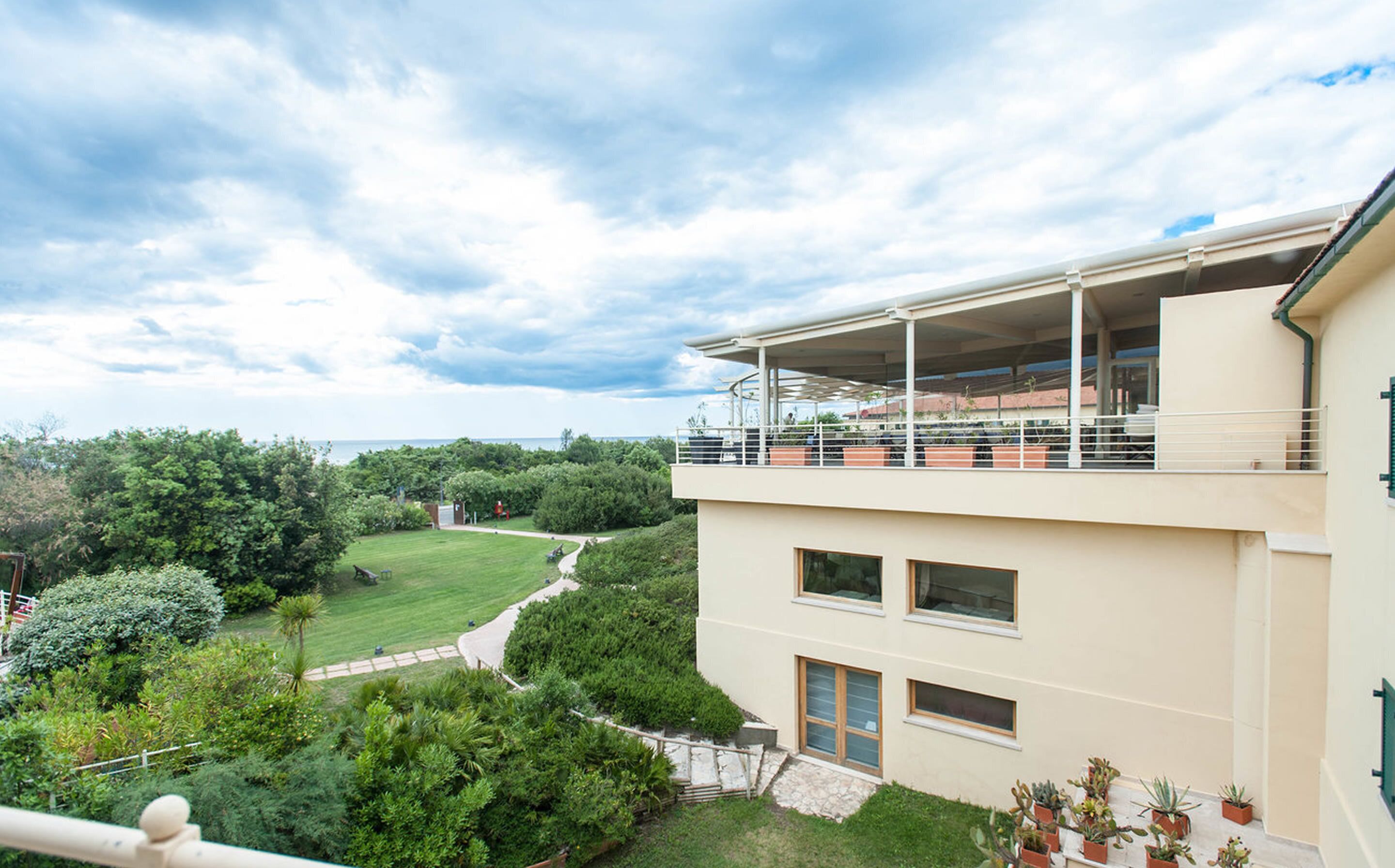 Un edificio moderno de dos plantas con un balcón que da a un exuberante jardín y vistas al mar.