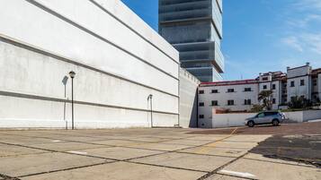 A parking area with a white building and a modern high-rise in the background.