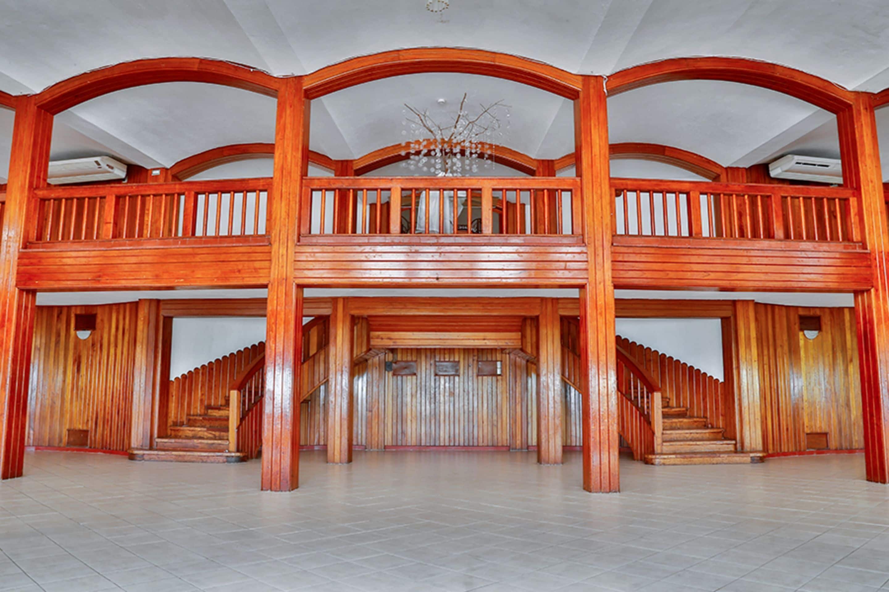 A spacious interior with a grand staircase leading to a mezzanine level, wooden railings, and a chandelier.