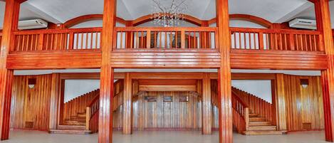 A spacious interior with a grand staircase leading to a mezzanine level, wooden railings, and a chandelier.