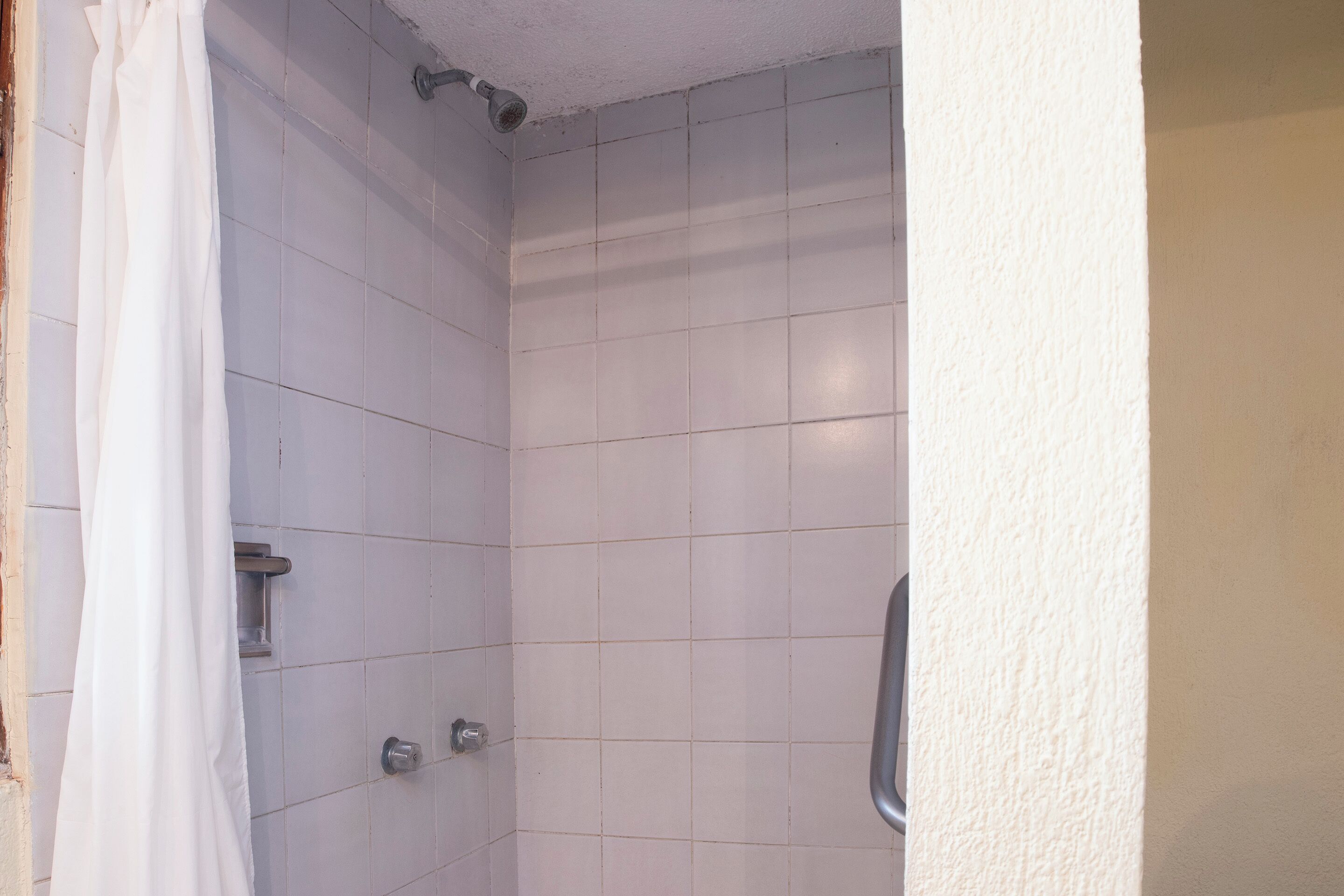 A small, tiled shower area with a shower curtain, a handheld showerhead, and a wall-mounted faucet.