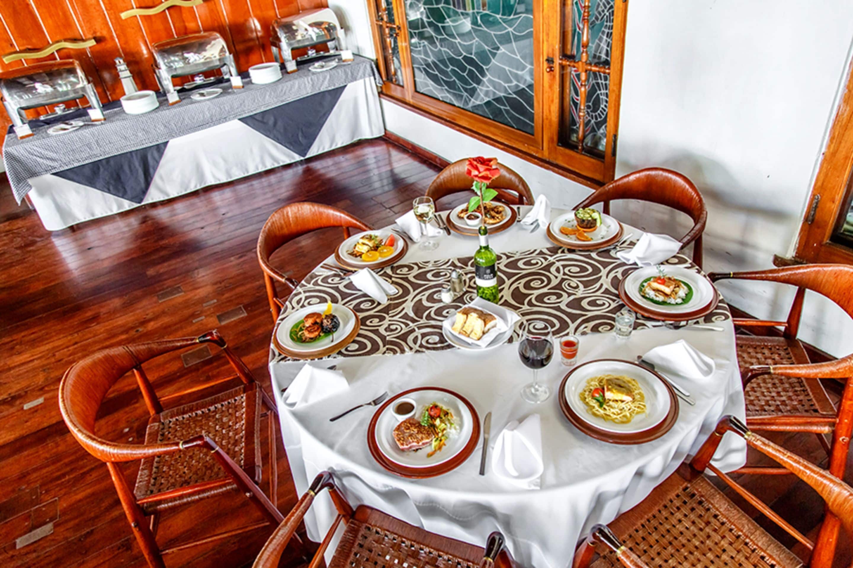 A dining area with a round table set for six, surrounded by wicker chairs.