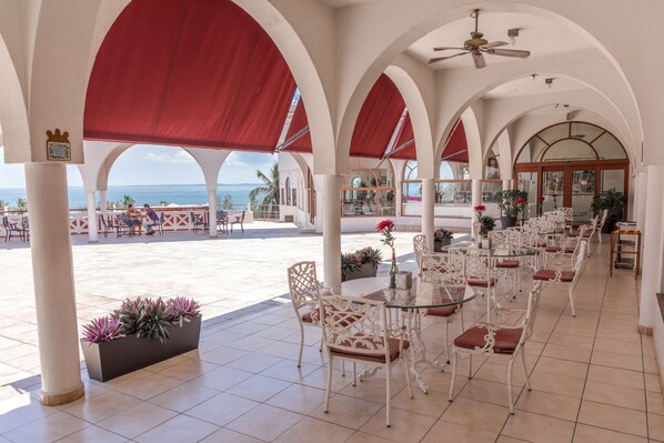 A covered outdoor seating area with white chairs and tables, red canopies, and a view of the ocean. - Collection O Hotel Mocambo, Boca del Río (Boca del Río)