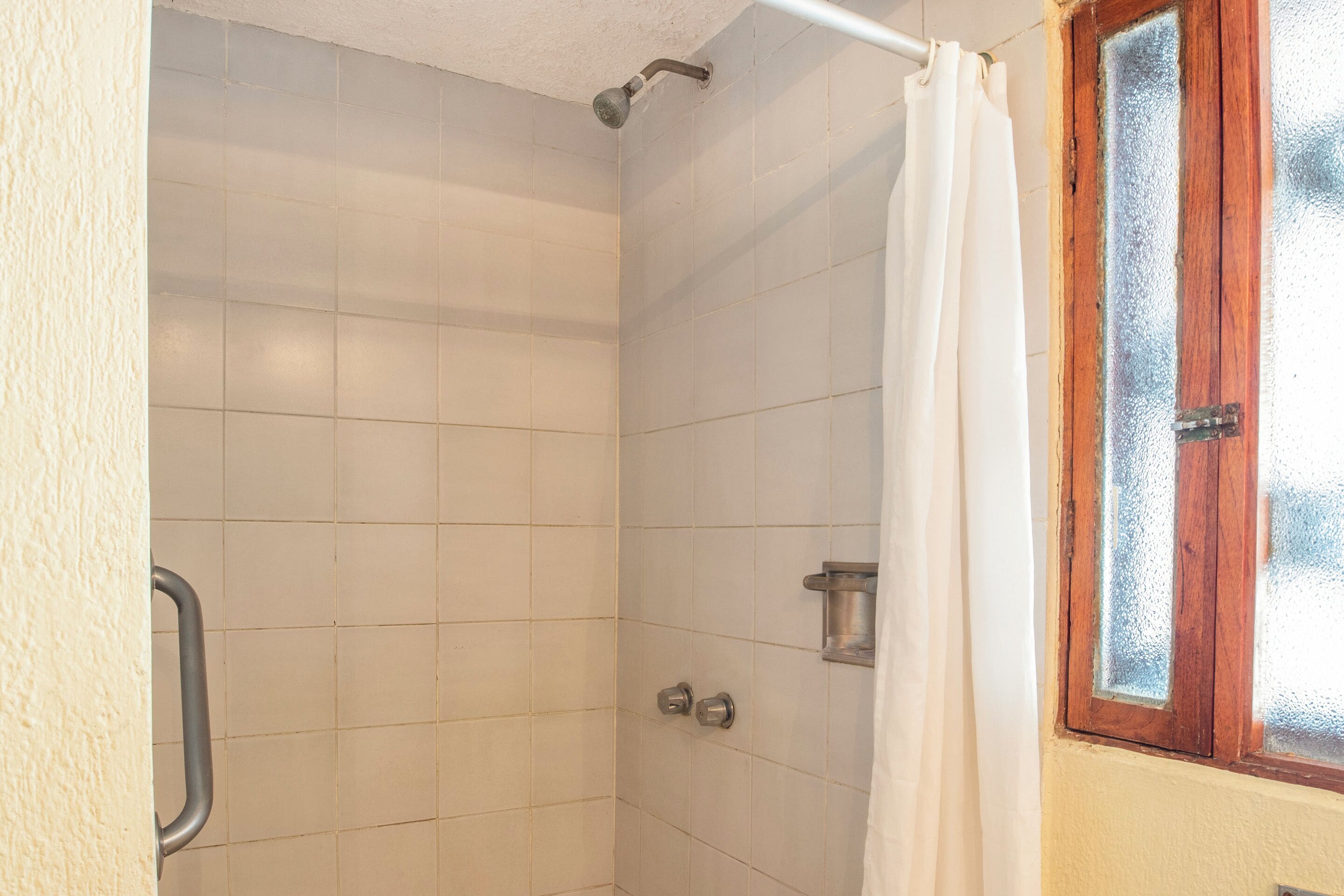 A shower with white tiles, a metal handle, and a glass door with a wooden frame.