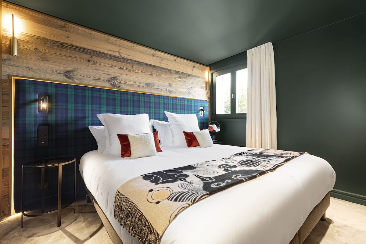 Quarto moderno com cabeceira de madeira, uma cama grande com lençóis brancos e um cobertor estampado.