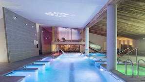 Una piscina interior moderna con múltiples carriles, techo de madera y una zona de estar al fondo.
