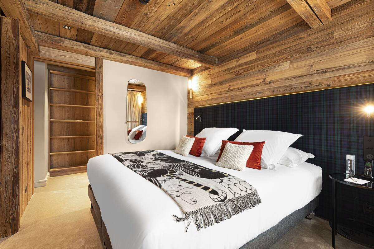 Quarto com teto de madeira, cama com roupa de cama branca, mesa de cabeceira com telefone e espelho na parede.
