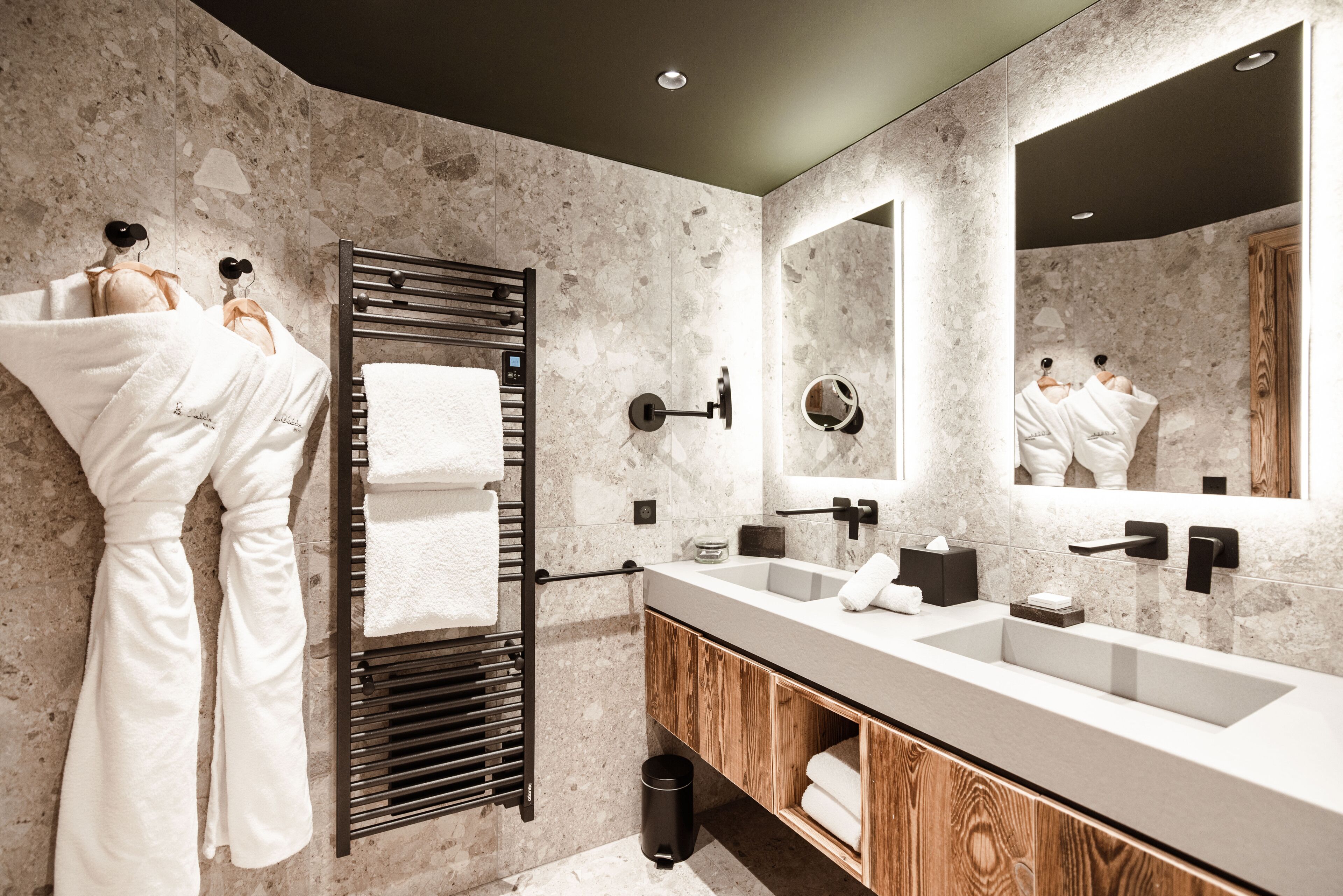 Une salle de bain moderne avec un grand miroir, deux lavabos et un porte-serviettes avec des peignoirs.
