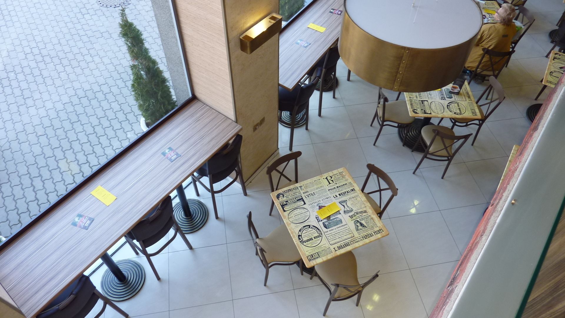 A restaurant with multiple tables and chairs, a tiled floor, and a view of the outside through large windows.