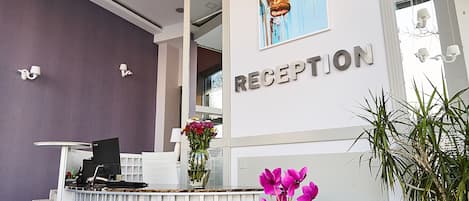 Un área de recepción con un escritorio, computadora y un florero con flores.