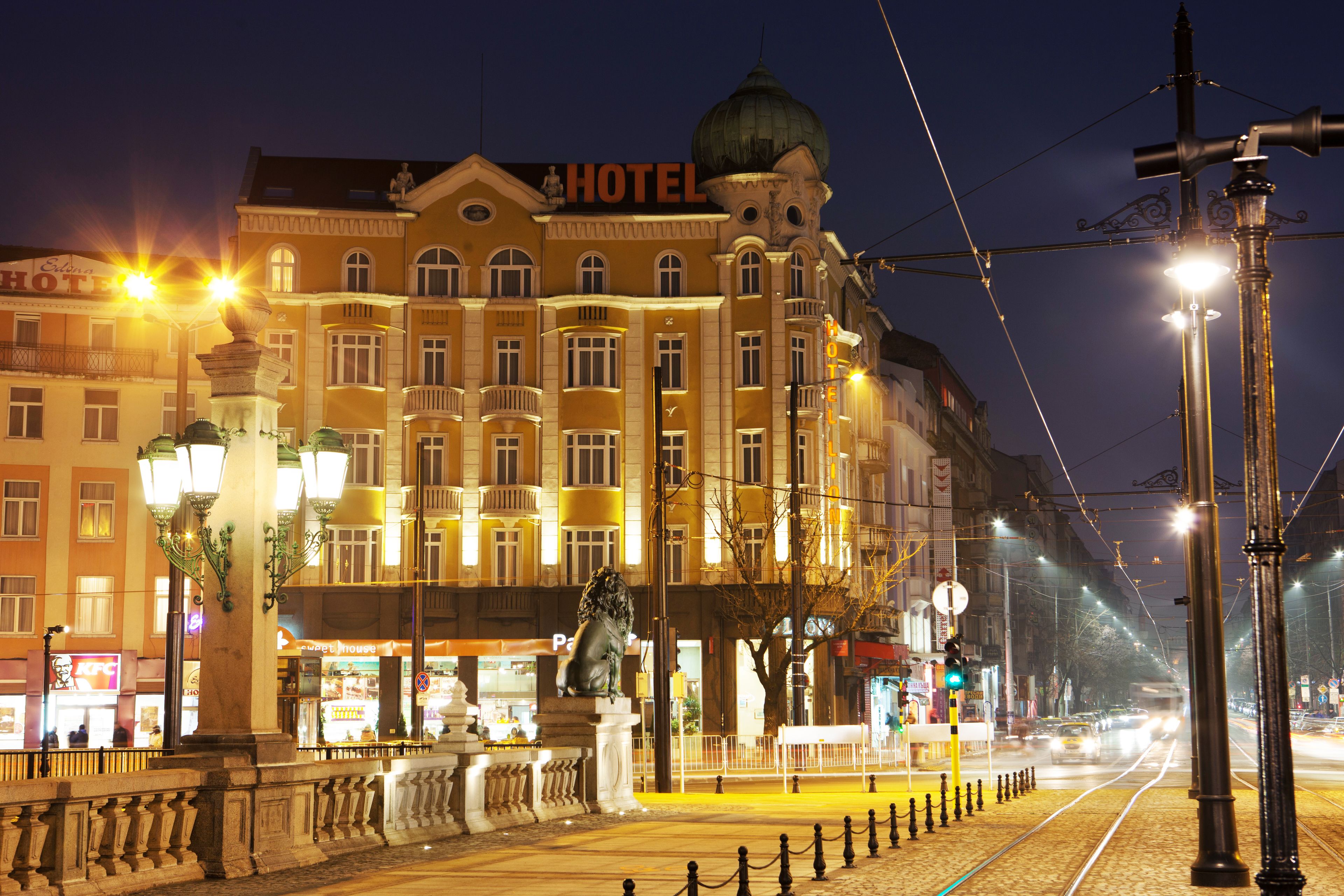 A hotel with a prominent sign, a statue in front, and a tram line nearby.