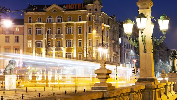 Um hotel com um letreiro chamativo 'HOTEL', uma estátua e luminárias ornamentais.