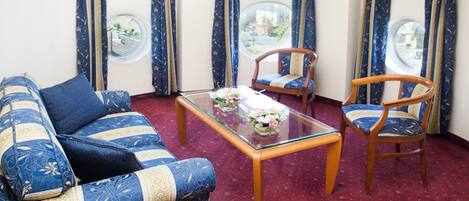 A room with a sofa, two chairs, a glass coffee table, and curtains with a view of the outside.