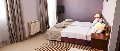 A hotel room with a bed, a bedside table with a lamp, a television, and a tray with fruits and a teapot.